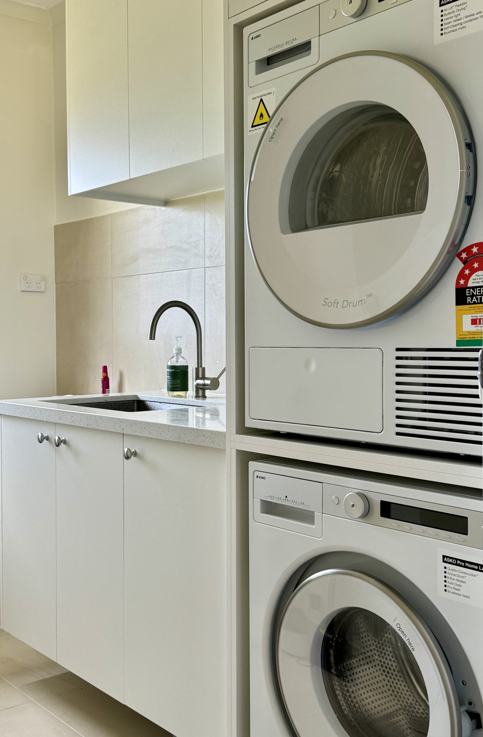 Modern laundry room with stacked washer and dryer, white cabinets, and a sink with a faucet. Modern laundry room with stacked washer and dryer, white cabinets, and a sink with a faucet.