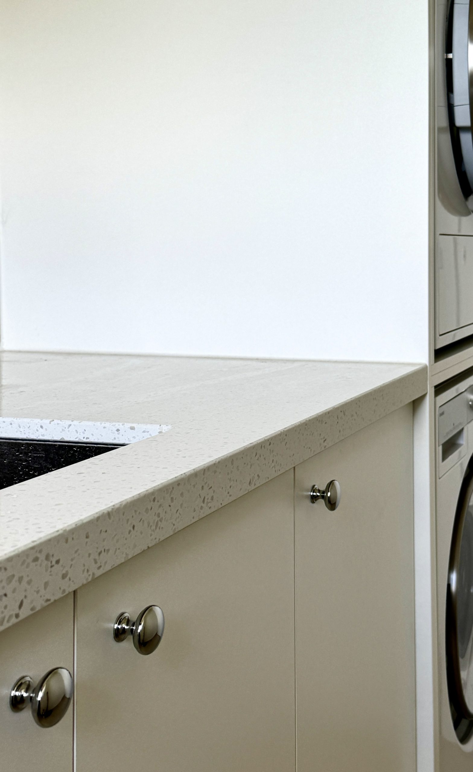 Minimalist kitchen with light beige cabinets, gray speckled countertop, silver knobs, and a side view of a washer-dryer. Minimalist kitchen with light beige cabinets, gray speckled countertop, silver knobs, and a side view of a washer-dryer.