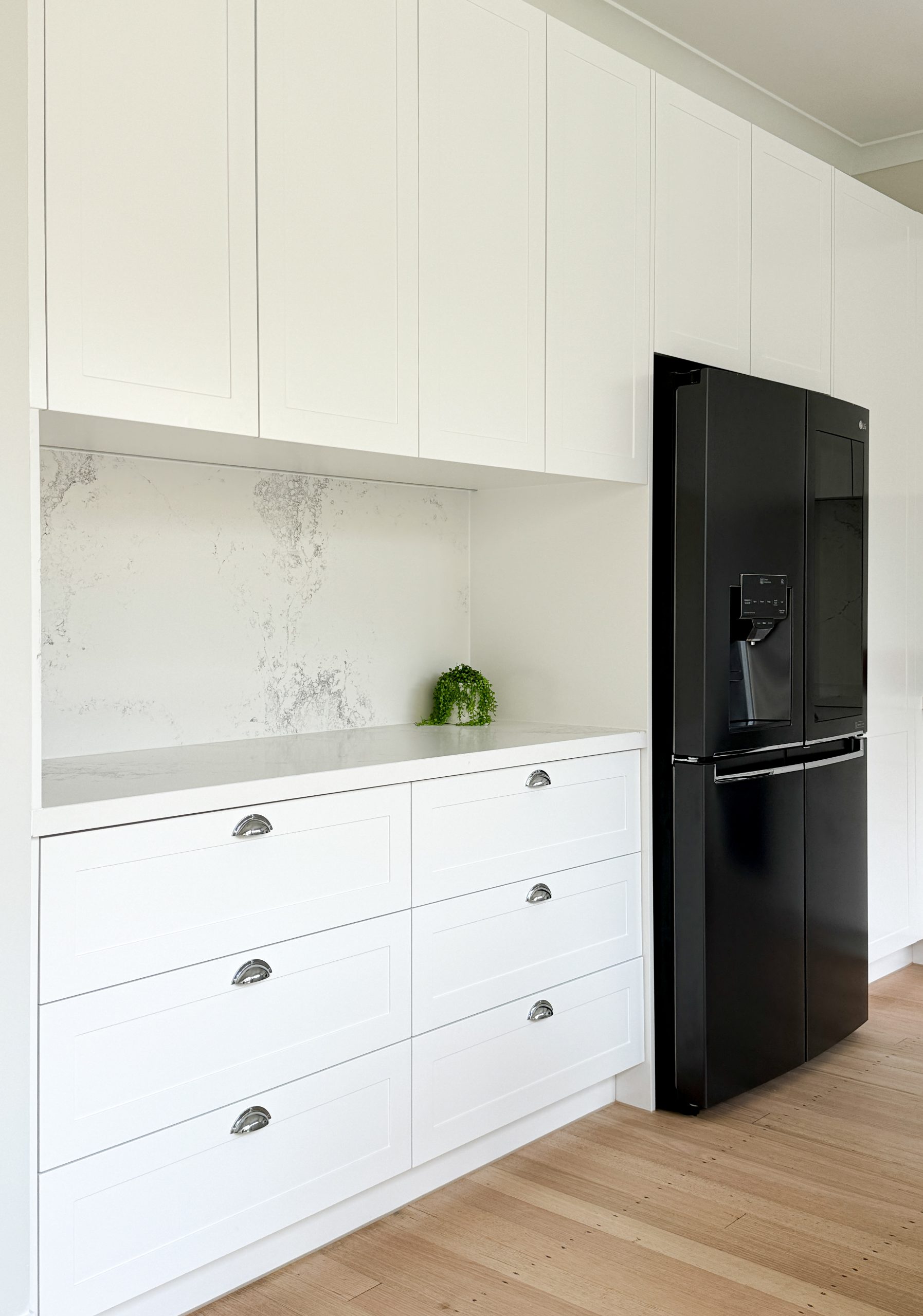 Minimalist kitchen with white cabinets, a black fridge, and a small green plant on the countertop. Minimalist kitchen with white cabinets, a black fridge, and a small green plant on the countertop.