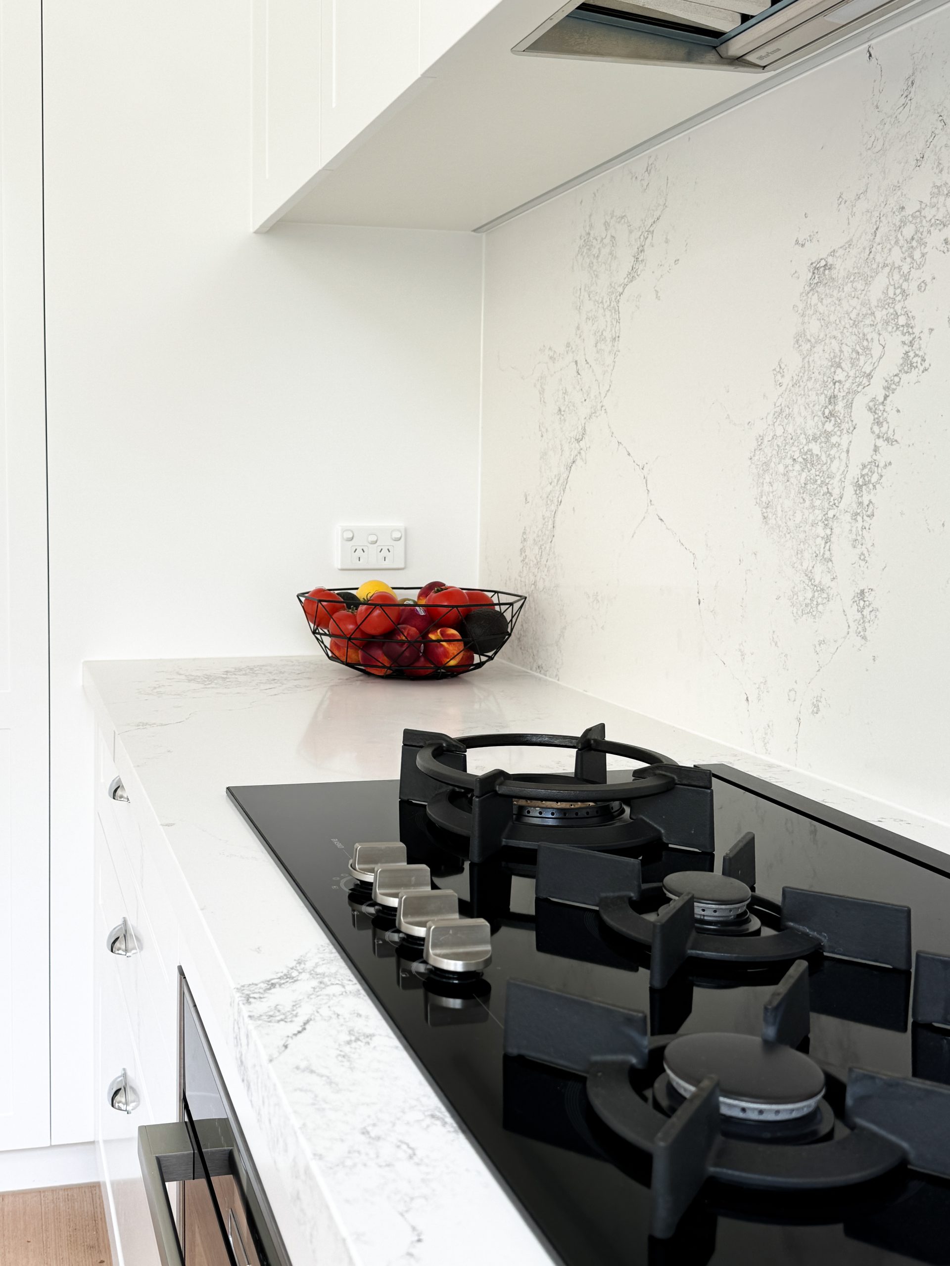 Modern kitchen with a sleek black stove. White marble countertops hold a metal fruit bowl filled with apples. Modern kitchen with a sleek black stove. White marble countertops hold a metal fruit bowl filled with apples.