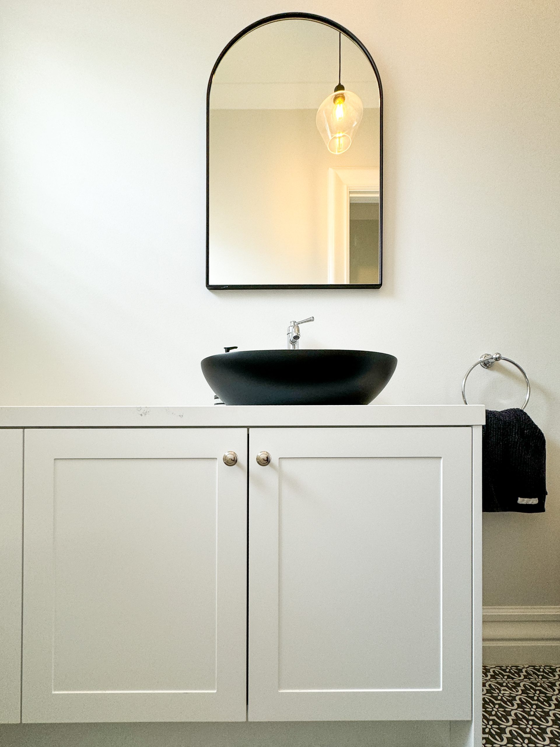 Minimalist bathroom with white cabinet, black countertop sink, arched mirror, and pendant light. Minimalist bathroom with white cabinet, black countertop sink, arched mirror, and pendant light.