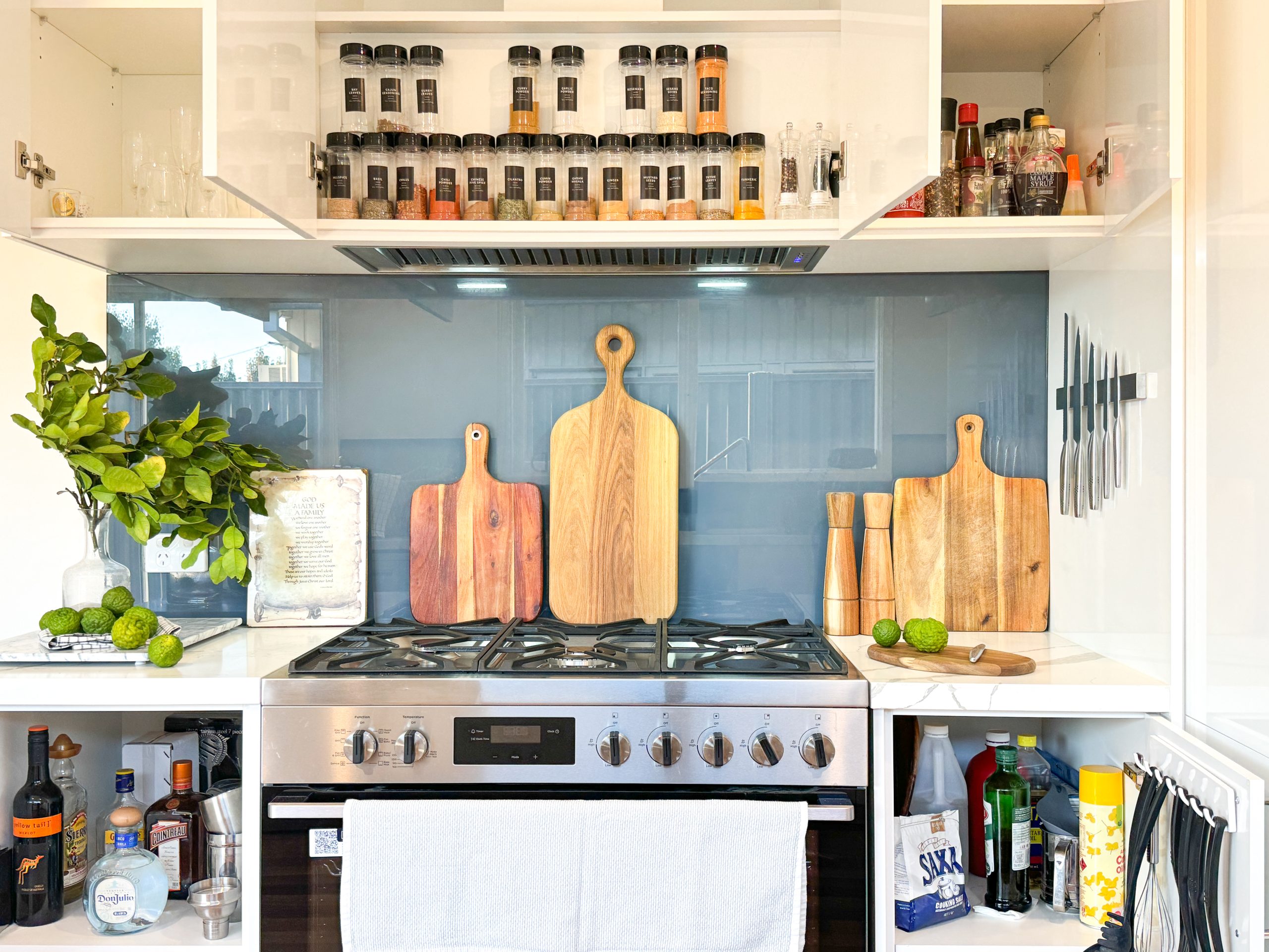 Modern kitchen with a stove, wooden cutting boards, knives, spice jars, and a leafy plant on the counter. Modern kitchen with a stove, wooden cutting boards, knives, spice jars, and a leafy plant on the counter.