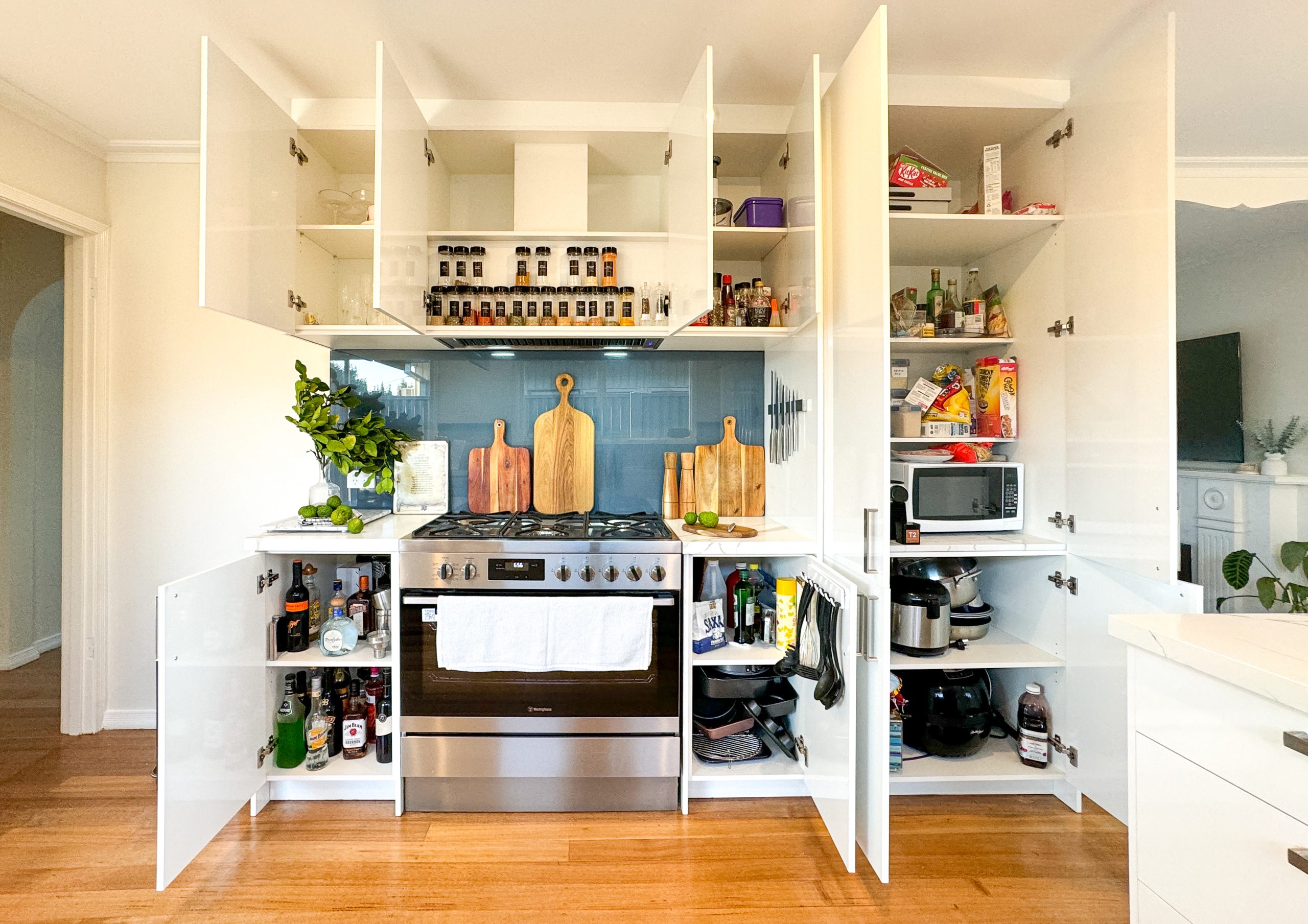 Bright kitchen with open cabinets showing spices, cutting boards, and various kitchen items around a stove. Bright kitchen with open cabinets showing spices, cutting boards, and various kitchen items around a stove.