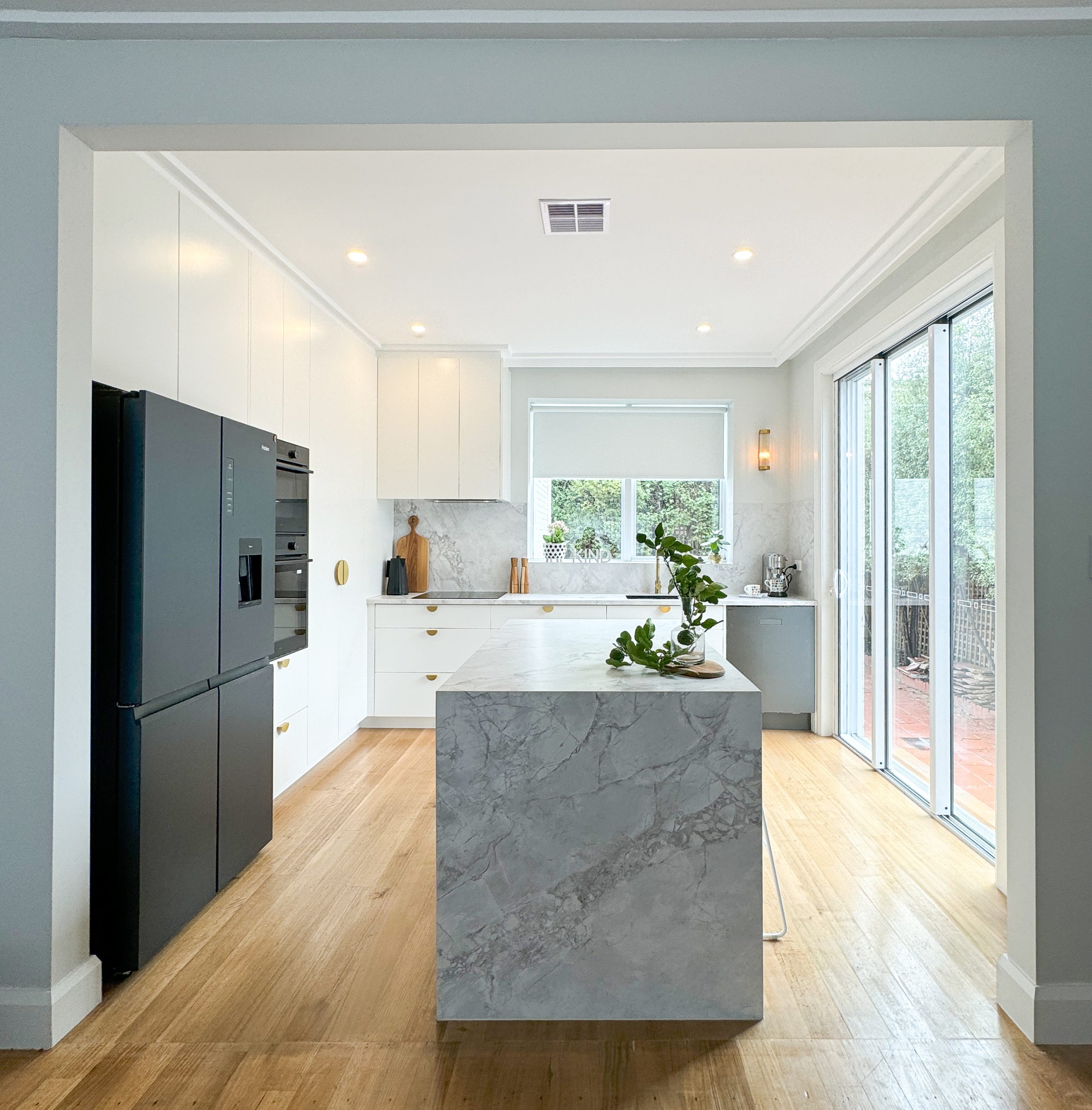 Modern kitchen with marble island, black fridge, white cabinets, wood flooring, and large sliding glass doors. Modern kitchen with marble island, black fridge, white cabinets, wood flooring, and large sliding glass doors.