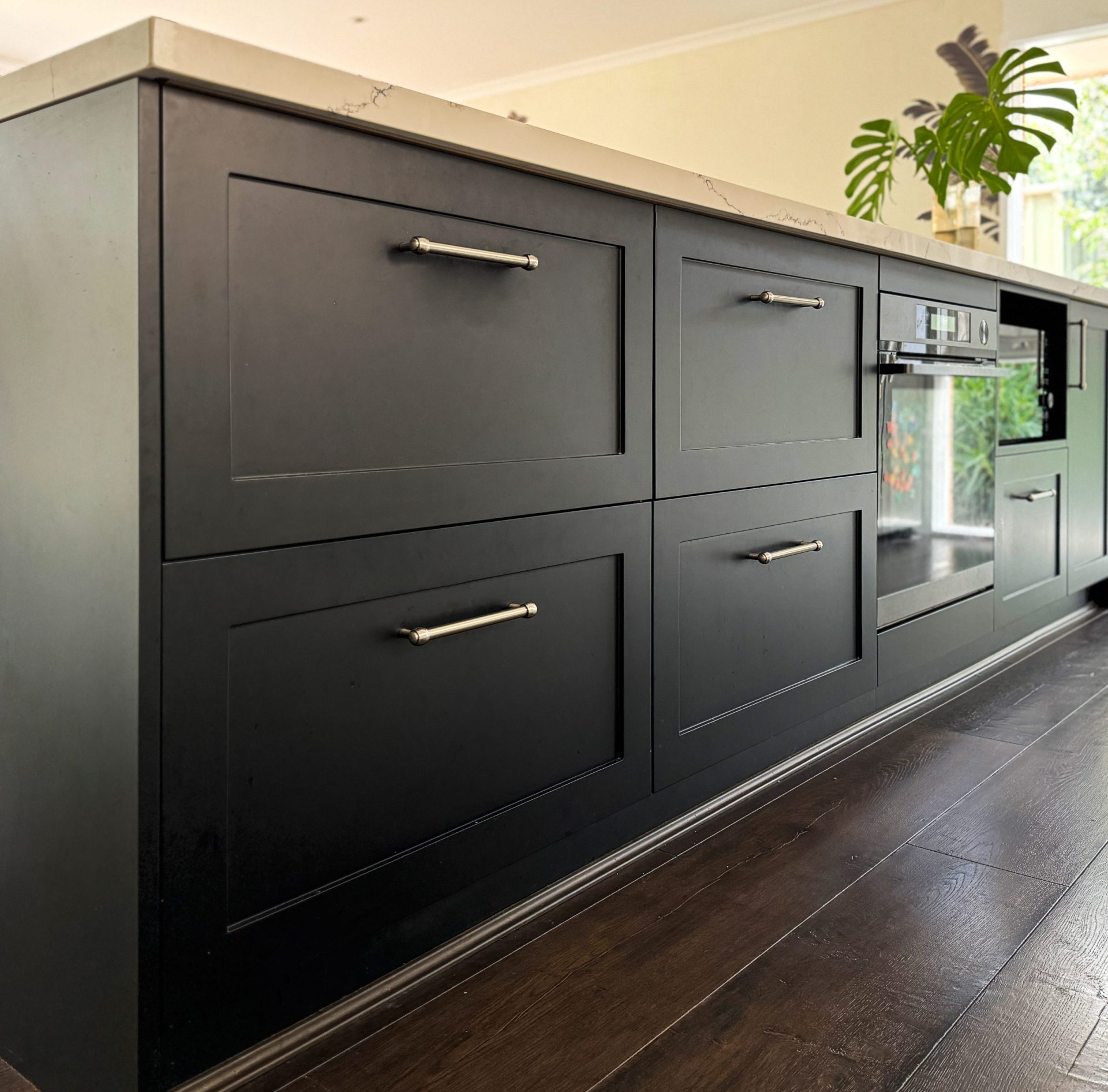 Black kitchen island with sleek cabinets, stainless steel handles, and a built-in oven, set on dark wood flooring. Black kitchen island with sleek cabinets, stainless steel handles, and a built-in oven, set on dark wood flooring.