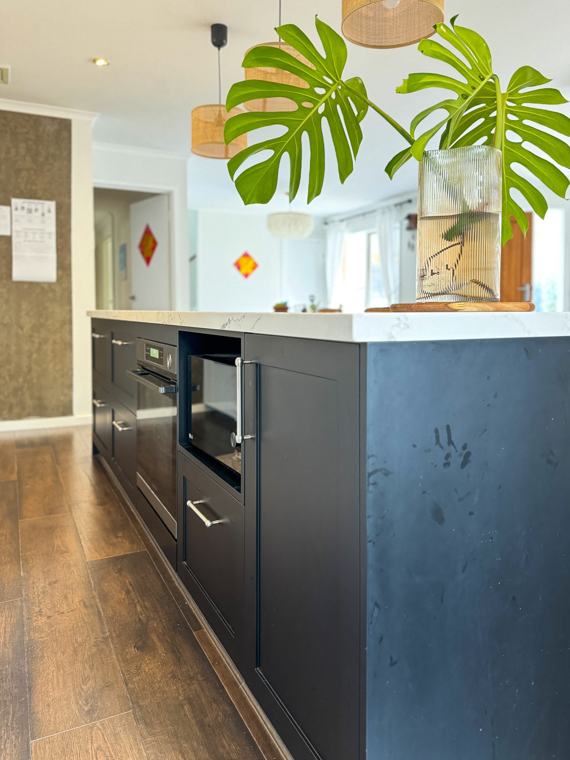 Modern kitchen island with dark cabinets, built-in oven, and a vase with large green leaves on top. Modern kitchen island with dark cabinets, built-in oven, and a vase with large green leaves on top.