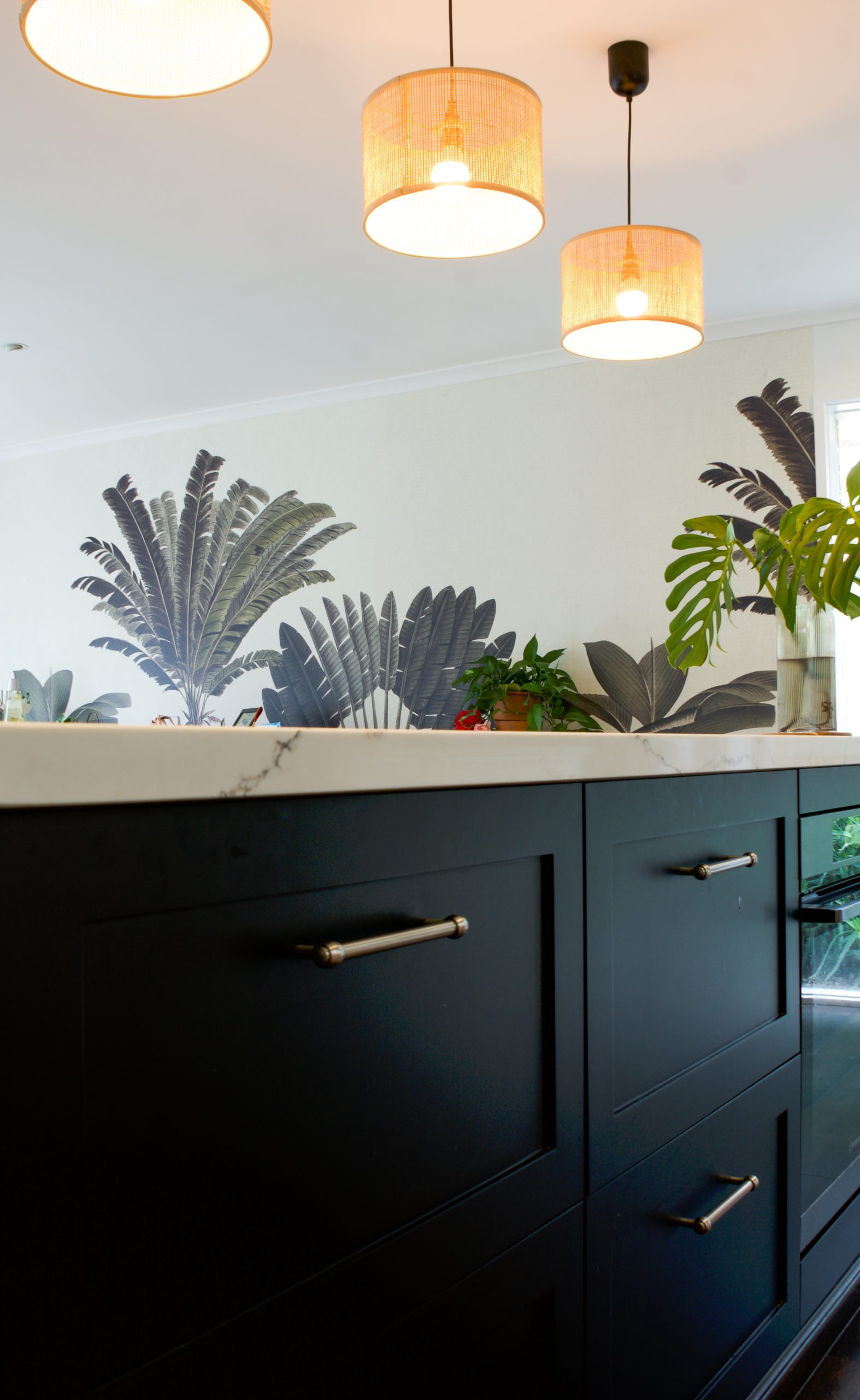 Modern kitchen with dark cabinets, overhead pendant lights, and tropical leaf decor on the wall. Modern kitchen with dark cabinets, overhead pendant lights, and tropical leaf decor on the wall.
