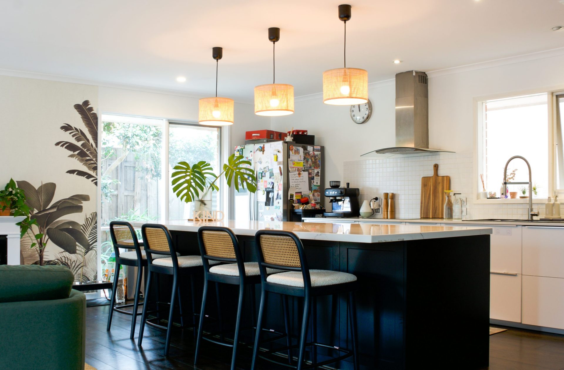 Modern kitchen with black island, four barstools, hanging lights, and a fridge covered in magnets and photos. Modern kitchen with black island, four barstools, hanging lights, and a fridge covered in magnets and photos.