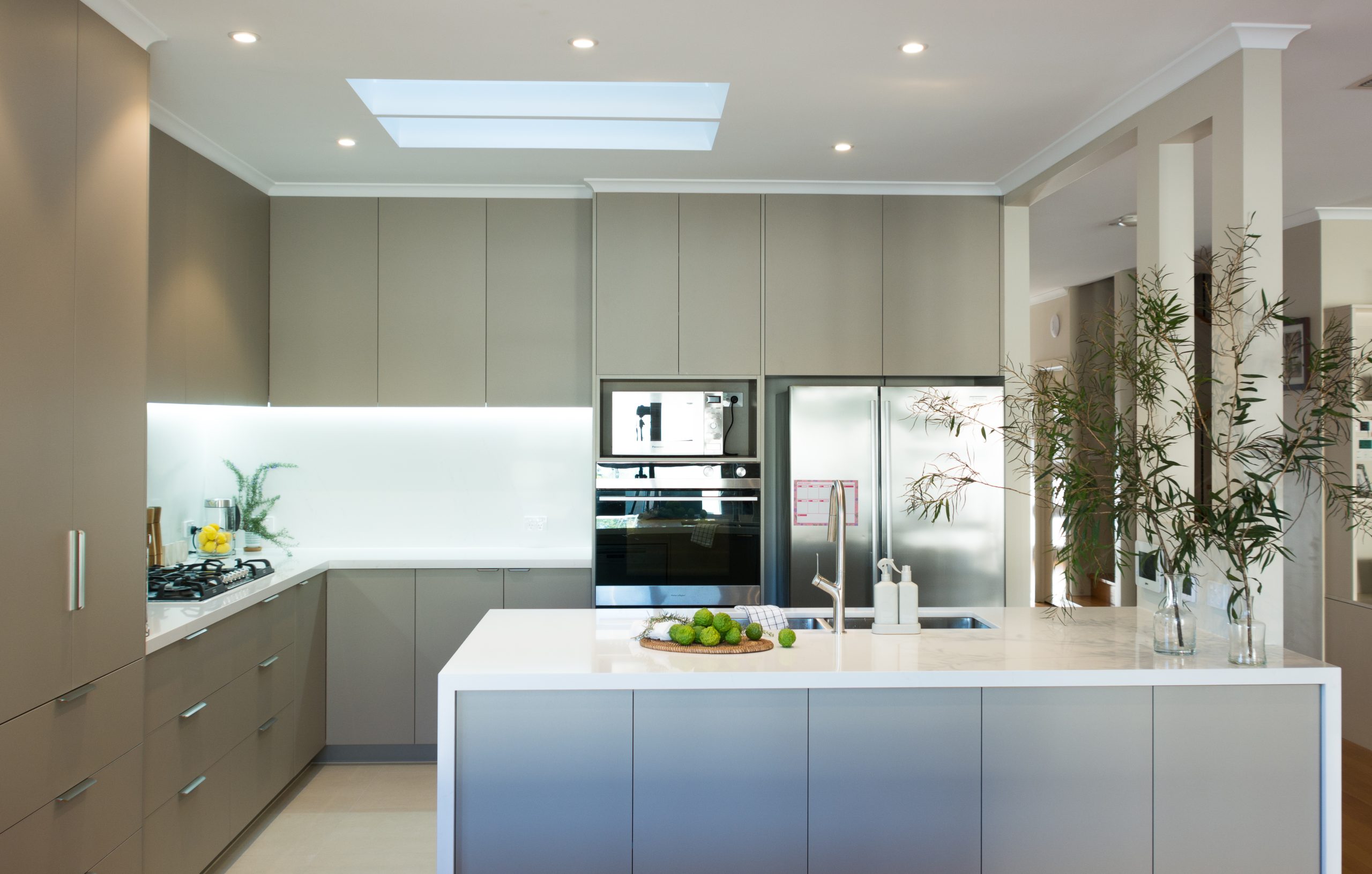 Modern kitchen with gray cabinets, skylight, stainless steel appliances, and a white island countertop with limes.