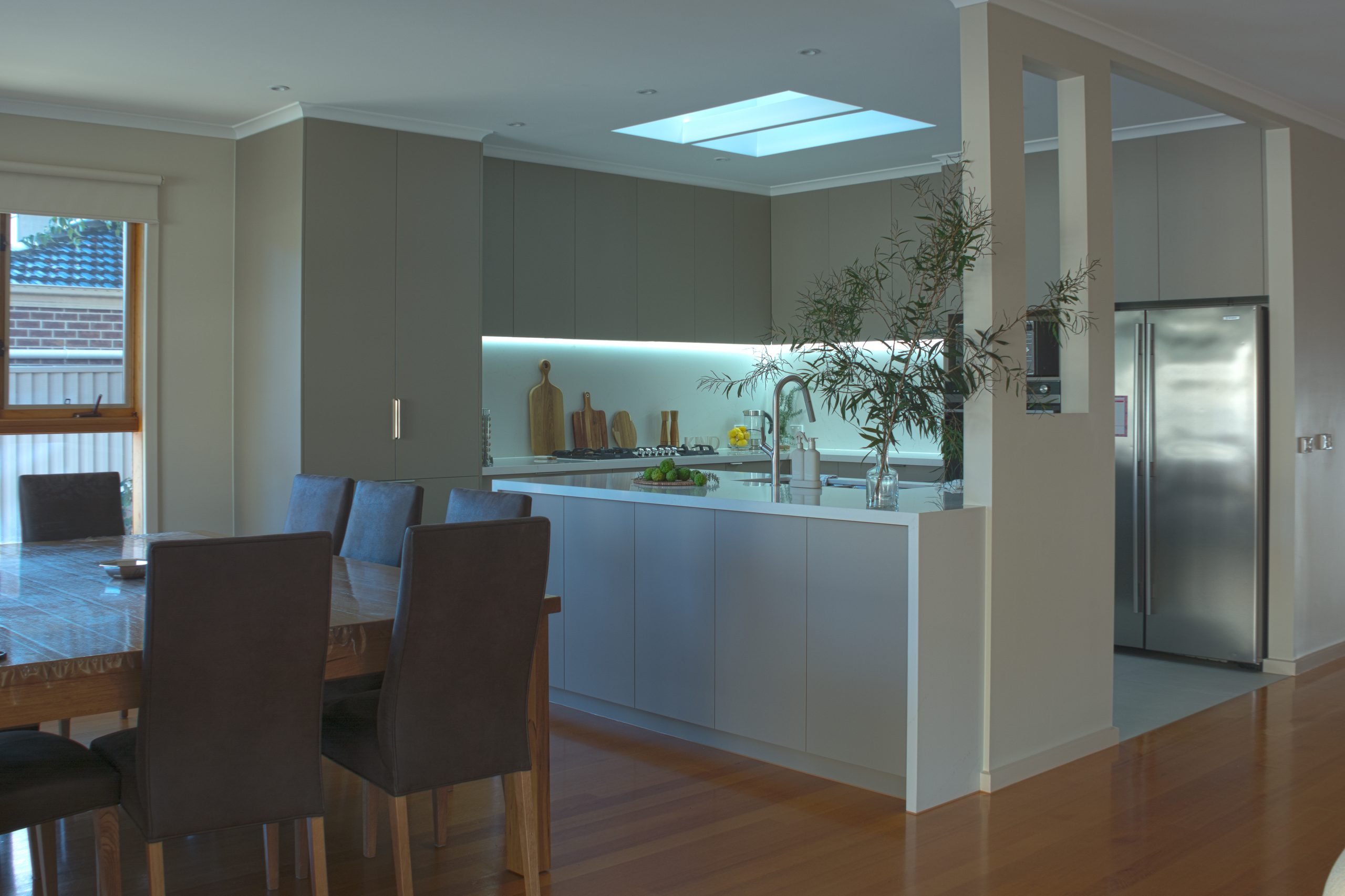 Modern kitchen with island, gray cabinets, dining table, plants, and skylight on wooden floor. Modern kitchen with island, gray cabinets, dining table, plants, and skylight on wooden floor.