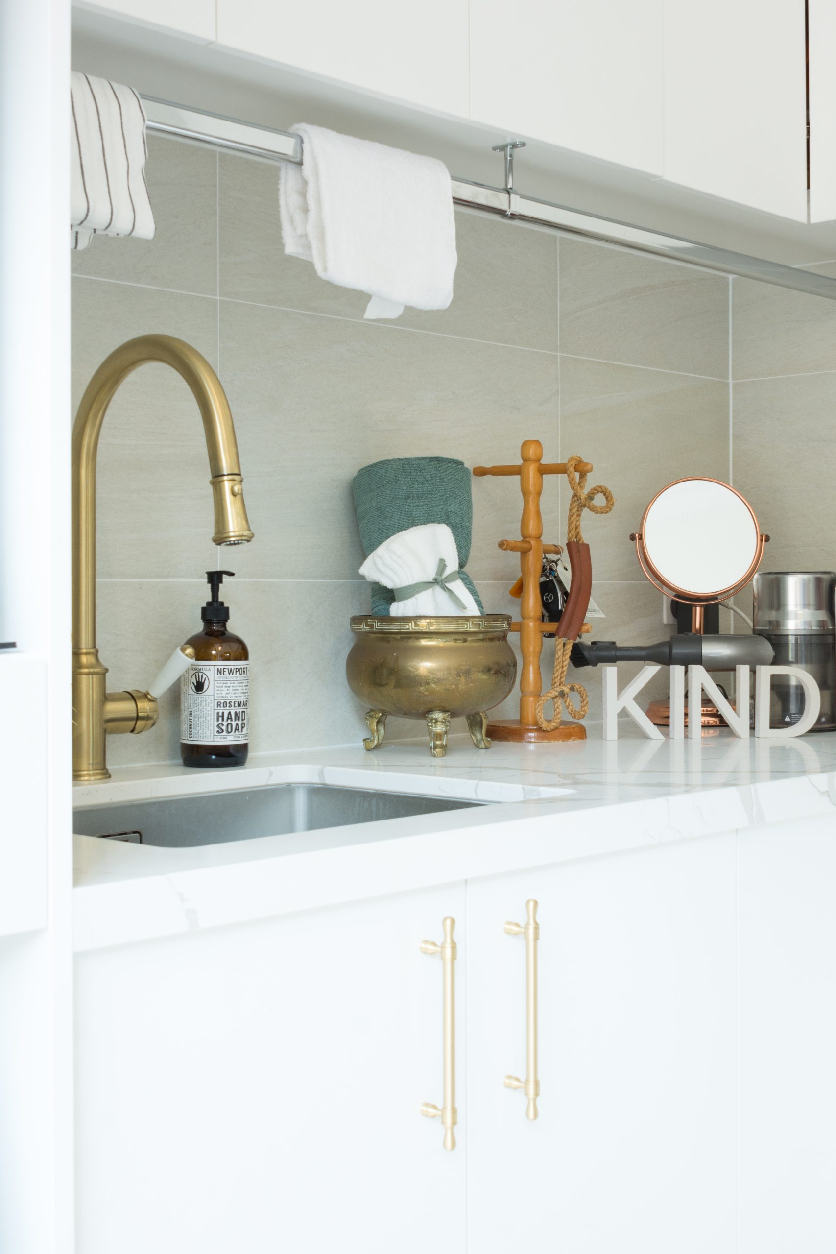 A kitchen sink with a gold faucet, beige tiles, and a counter with soap and decorative items. A kitchen sink with a gold faucet, beige tiles, and a counter with soap and decorative items.