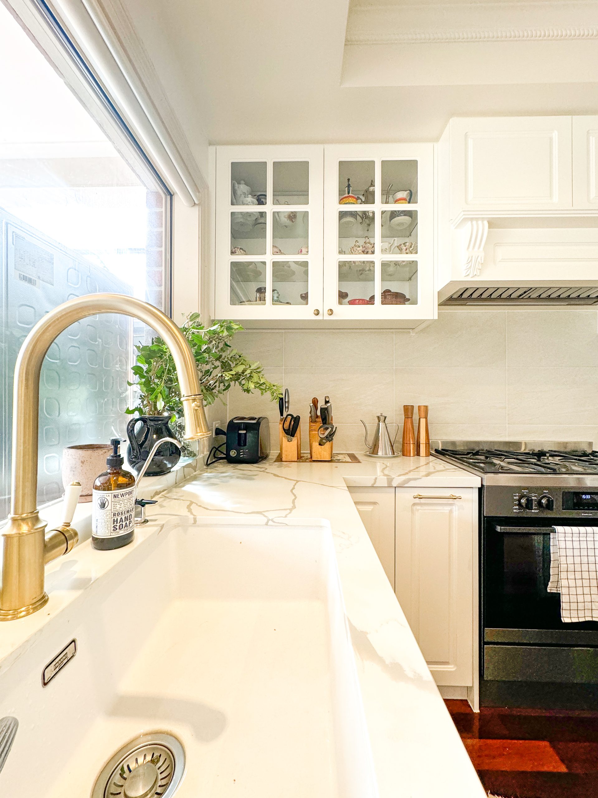 Bright kitchen with white cabinets, a marble countertop, brass faucet, potted plant, and modern appliances. Bright kitchen with white cabinets, a marble countertop, brass faucet, potted plant, and modern appliances.