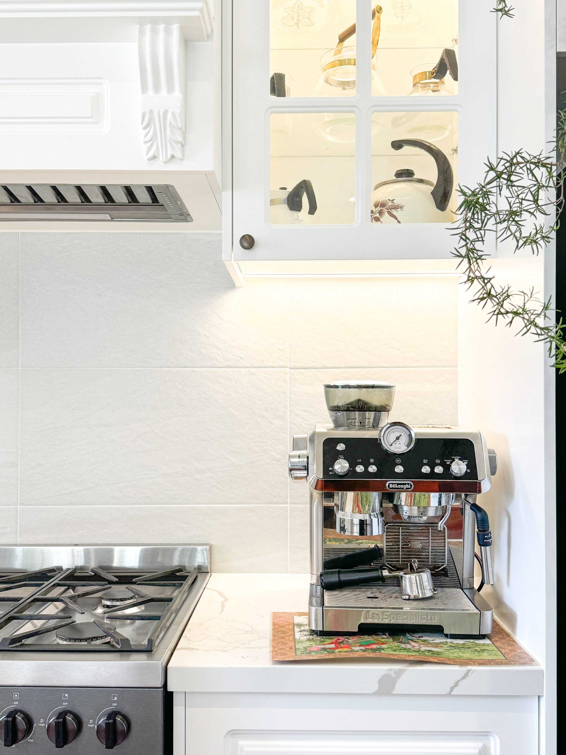 Kitchen corner with a coffee machine on the counter, next to a stove and a cabinet displaying utensils above. Kitchen corner with a coffee machine on the counter, next to a stove and a cabinet displaying utensils above.