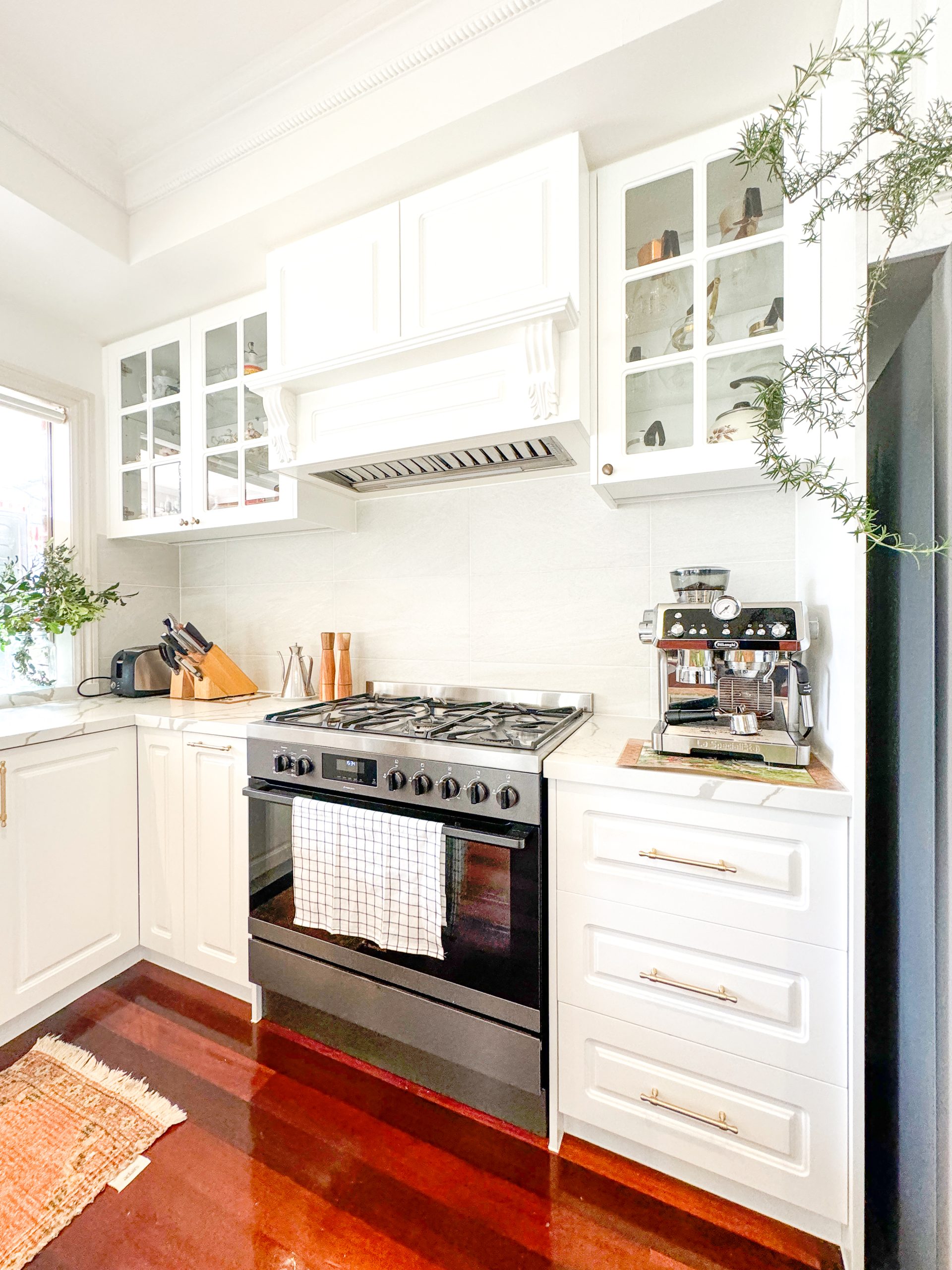 Bright kitchen with white cabinets, black stove, and coffee machine. Wooden floor, plants near window and countertop. Bright kitchen with white cabinets, black stove, and coffee machine. Wooden floor, plants near window and countertop.