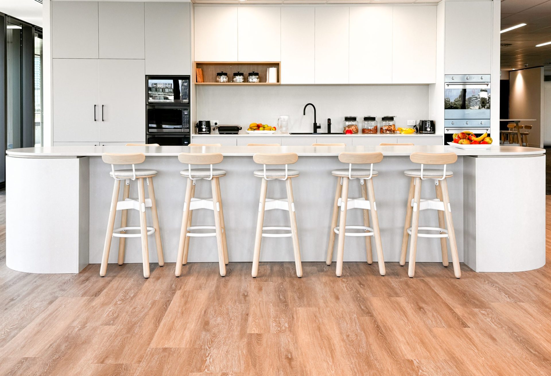 Modern kitchen with wooden stools at a white counter, white cabinets, and various kitchen appliances. Modern kitchen with wooden stools at a white counter, white cabinets, and various kitchen appliances.