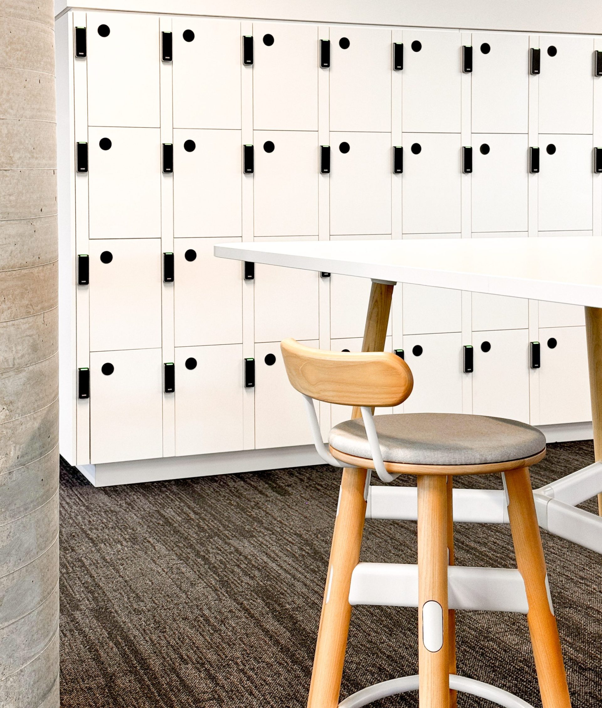 Wooden stool at a high table in front of white lockers with black handles in an office space. Wooden stool at a high table in front of white lockers with black handles in an office space.