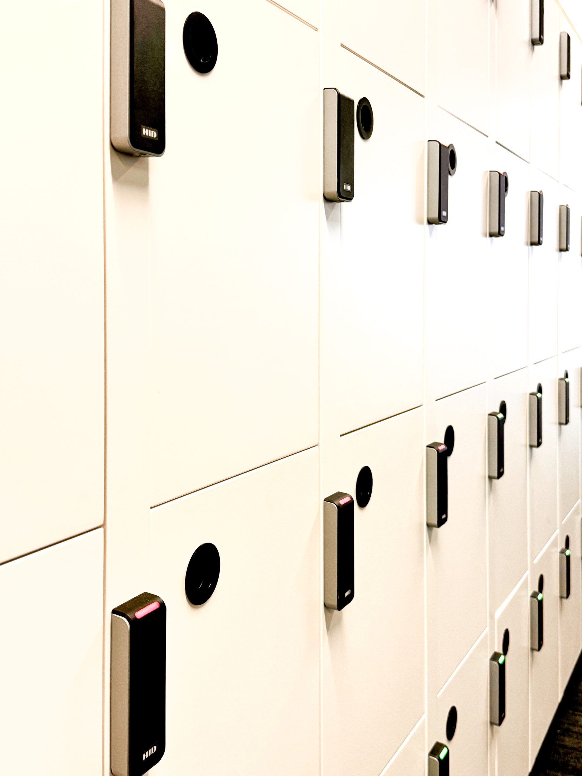 Rows of secure white lockers equipped with electronic locks and small circular black buttons. Rows of secure white lockers equipped with electronic locks and small circular black buttons.