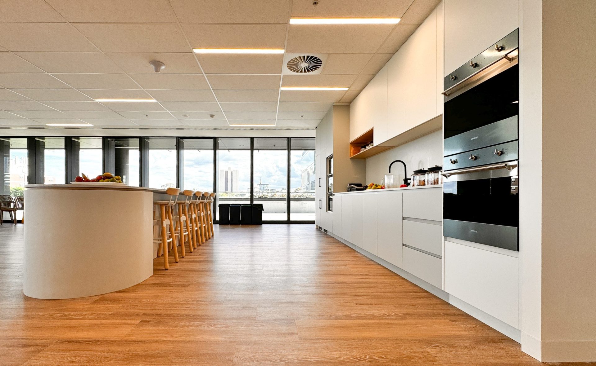 Modern kitchen with white cabinets, a long island with seating, and large windows overlooking a cityscape. Modern kitchen with white cabinets, a long island with seating, and large windows overlooking a cityscape.