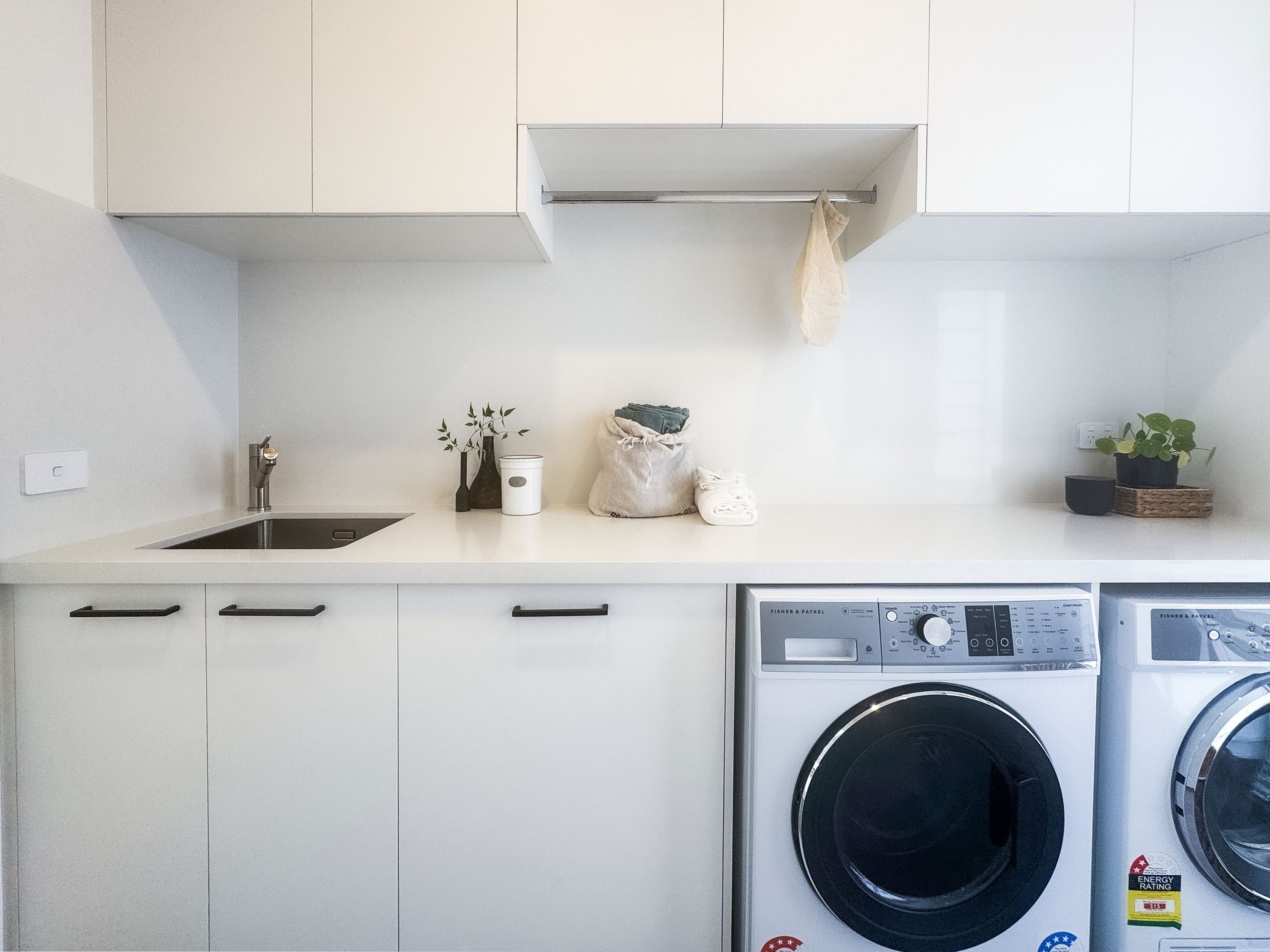 Custom laundry renovation in Hampton with white cabinetry, drying rail and integrated sink Custom laundry renovation in Hampton with white cabinetry, drying rail and integrated sink