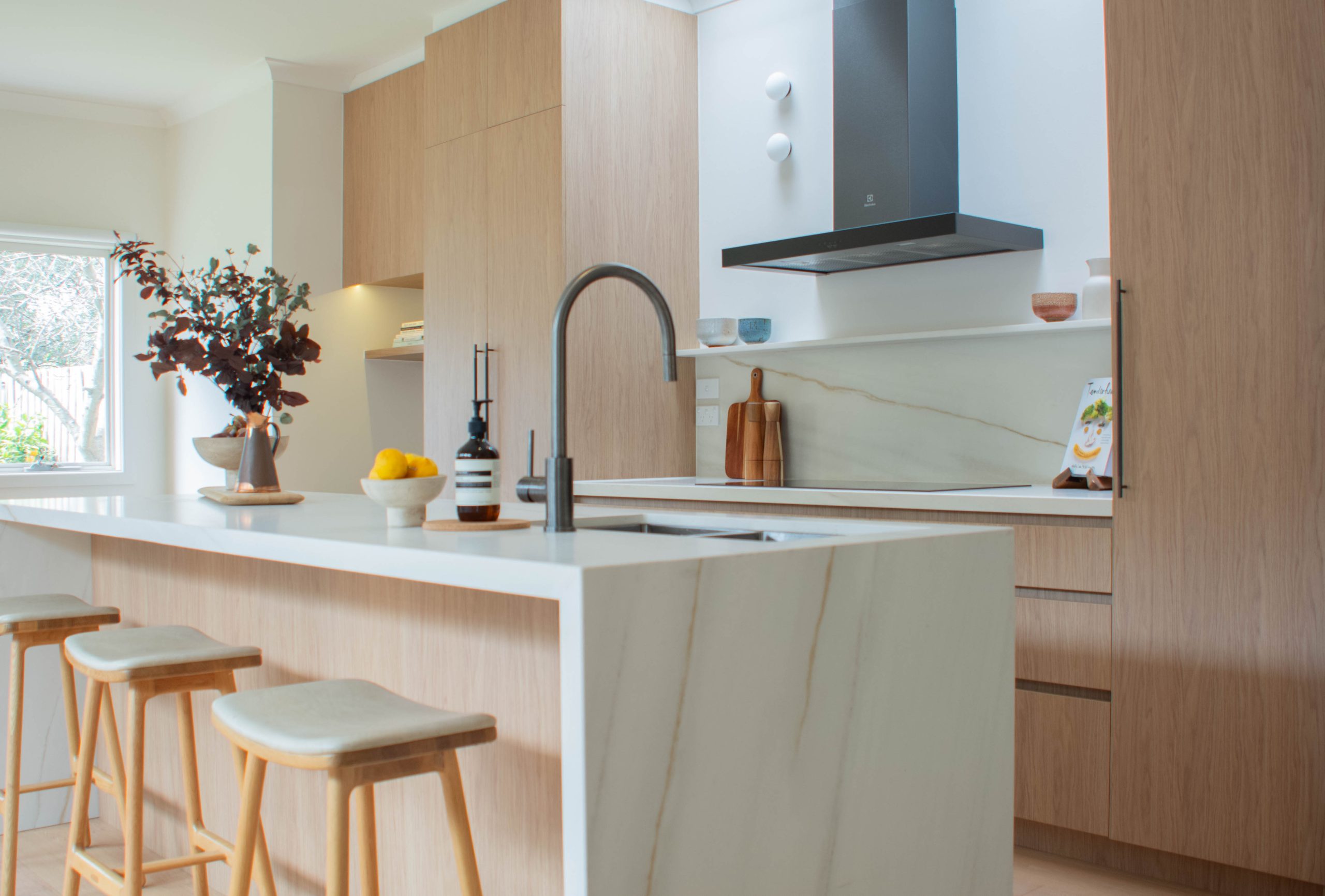Timber veneer kitchen with marble waterfall island bench, black rangehood and bar stools Timber veneer kitchen with marble waterfall island bench, black rangehood and bar stools